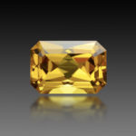 Golden yellow color natural heliodor beryl emerald cut, shaped loose gemstone setting for making jewelry. Eye clean, transparent with some small inclusions stone on black gradient background. Blur